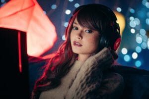 A woman wearing headphones poses indoors with a cozy setting, ideal for gaming themes.
