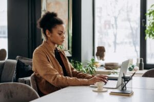 Focused woman typing on a laptop in a modern workspace with natural light.