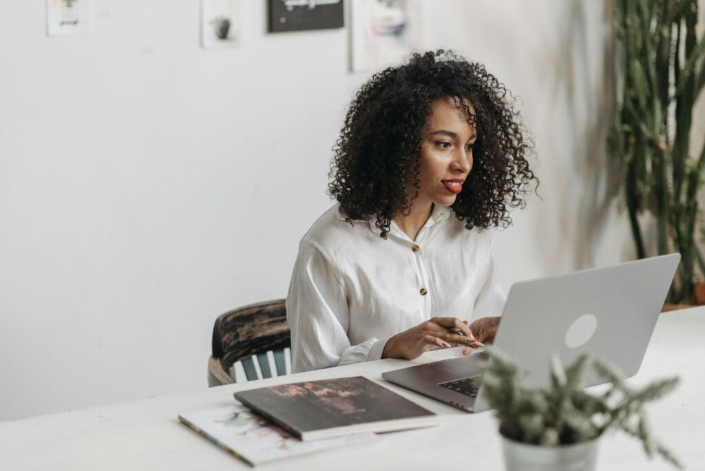 An African American woman with curly hair works attentively on a laptop in a modern office setting.