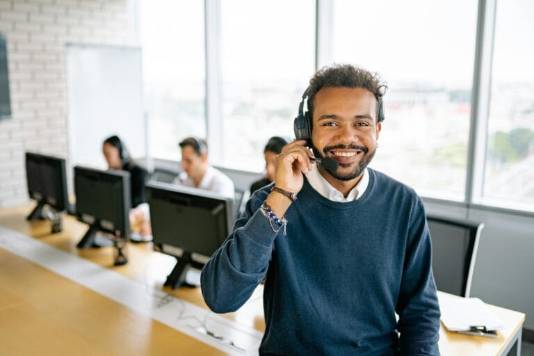 Cheerful male call center agent with headset in a bright office environment.