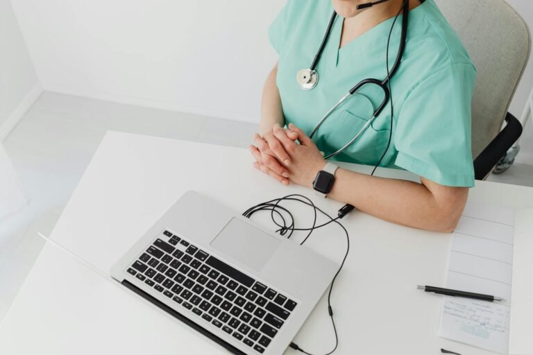 Doctor in scrubs with stethoscope conducting online consultation using a laptop.