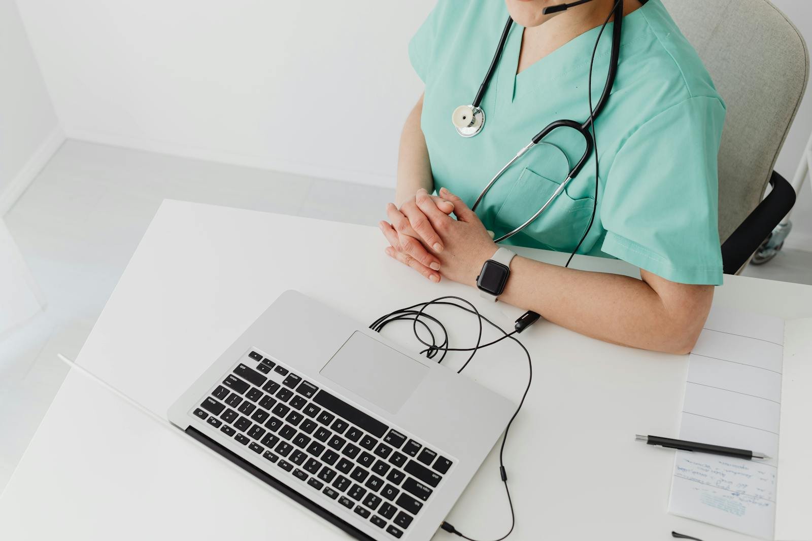 Doctor in scrubs with stethoscope conducting online consultation using a laptop.