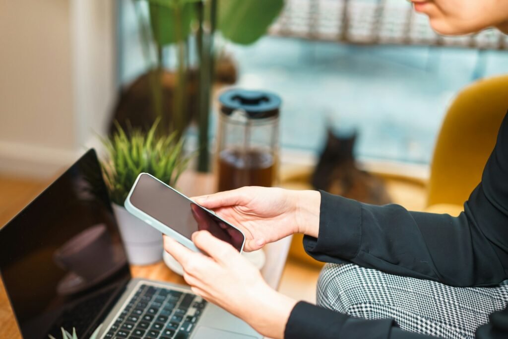 Person using a smartphone while working on a laptop.