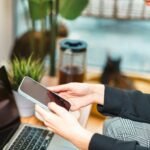 Person using a smartphone while working on a laptop.