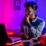 a person sitting at a desk with a laptop and a computer