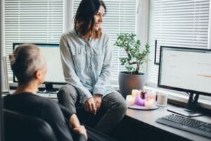 A Smiling Couple Converses In A Cozy Home Office With Candles And Computers.