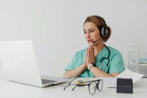 Female Nurse Using Telemedicine For A Virtual Consultation On A Laptop, Wearing Headphones And Stethoscope.