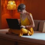 Senior woman in comfortable attire using a laptop in a warm, indoor setting, showcasing modern technology and leisure.
