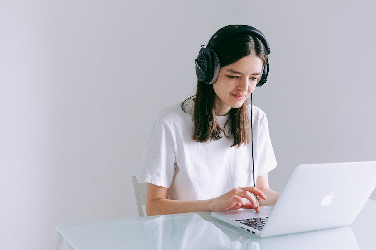 Young Woman Using Laptop With Headphones, Working Remotely In A Home Office.