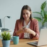 Young woman smiling while using her smartphone at desk.