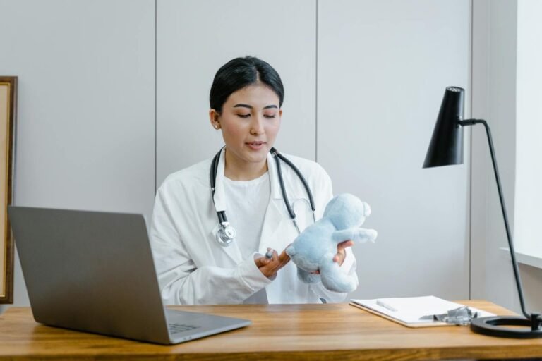 Female Doctor In Office Holding Teddy Bear During A Video Call Session.
