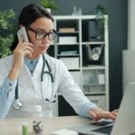 Doctor on phone, working on laptop in office.