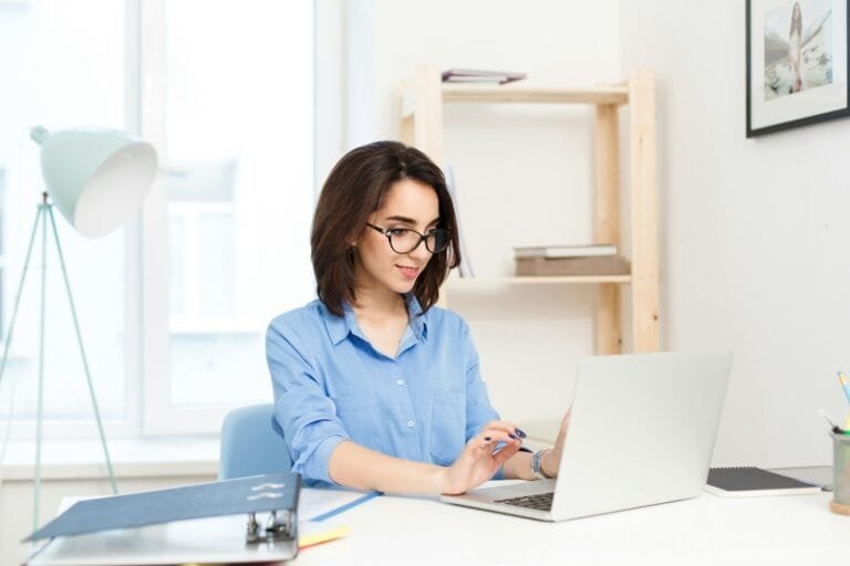 A Woman Sitting At A Desk Working On A Laptop