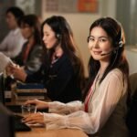 A smiling woman wearing a headset at a computer.